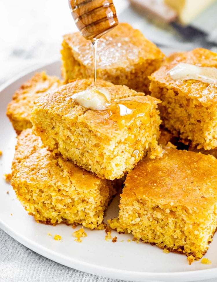 pieces of cornbread stacked on a plate with honey being drizzled over them