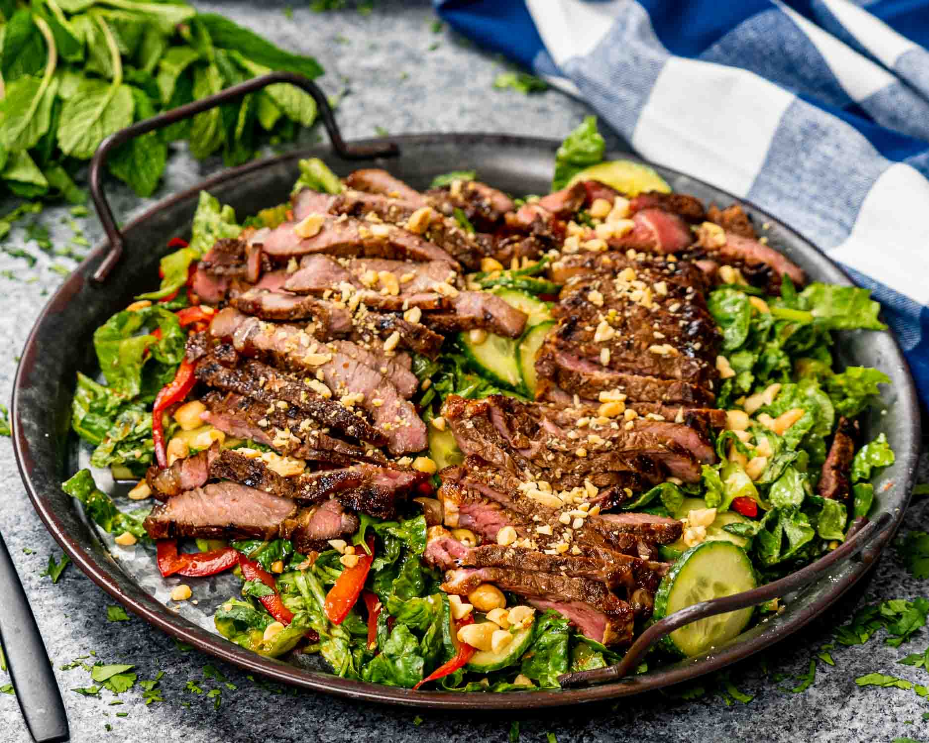 thai steak salad on a black platter garnished with some peanuts and a couple thai red chili peppers.