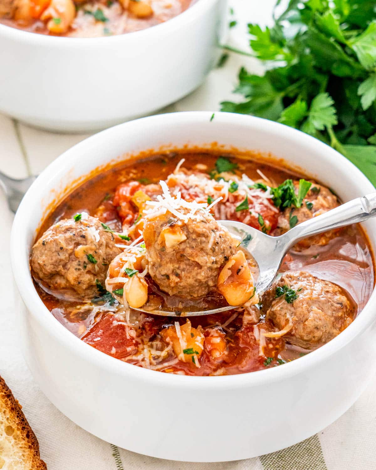 a spoon holding a meatball over a bowl loaded with soup