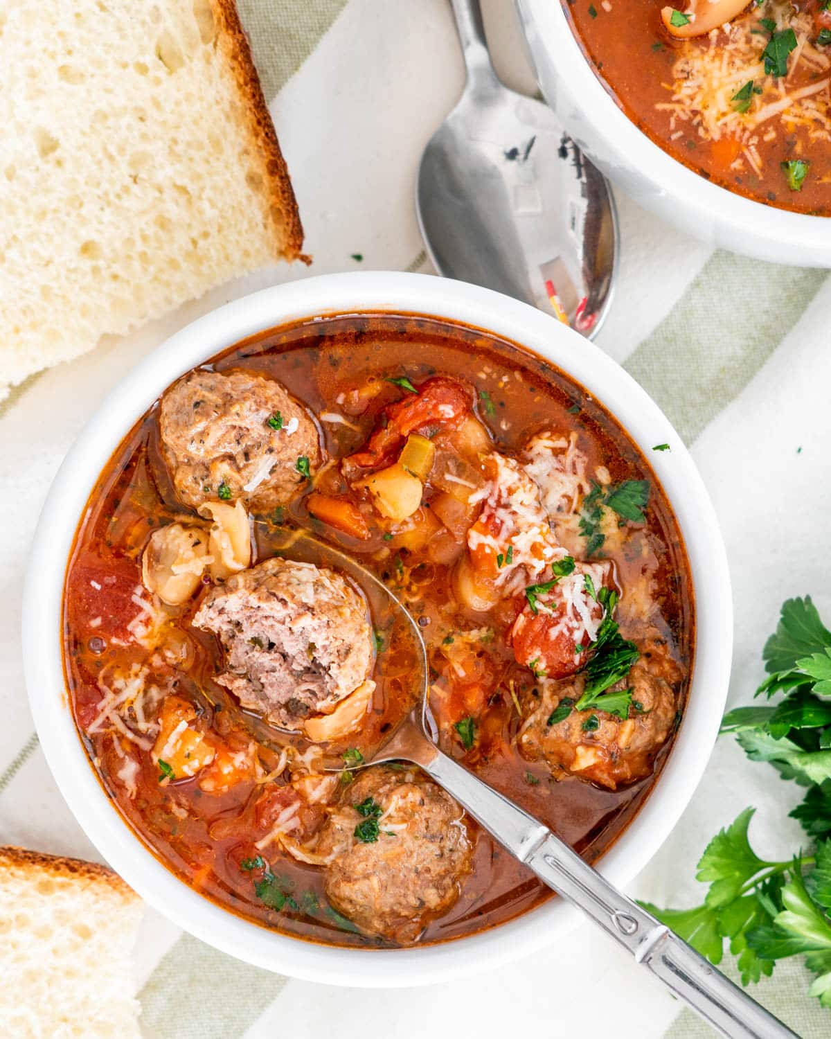 overhead shot of italian meatball soup in a white bowl with a spoon holding a meatball