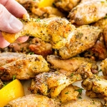 a hand holding up a lemon pepper wing with the other wings in the background