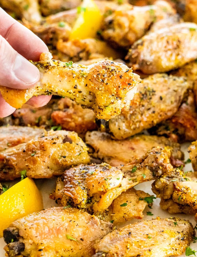 a hand holding up a lemon pepper wing with the other wings in the background