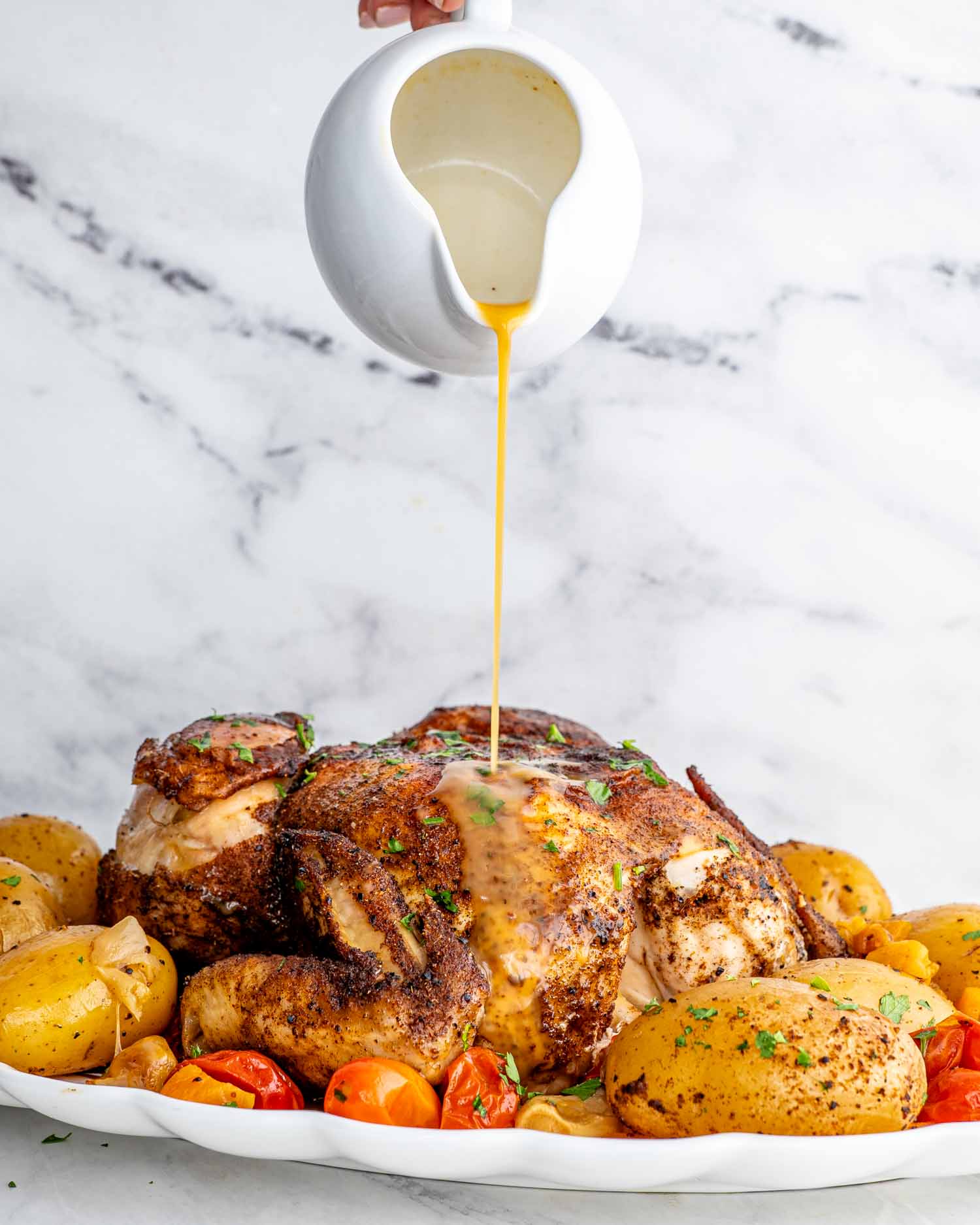 a hand pouring gravy over moroccan roast chicken and potatoes.