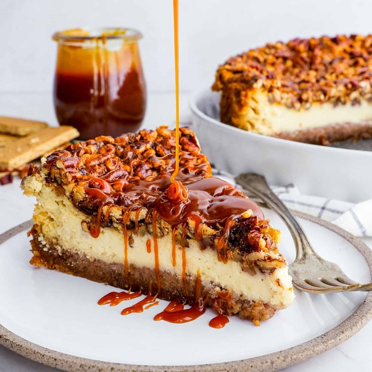 a slice of pecan pie cheesecake drizzled with caramel topping on a white plate.