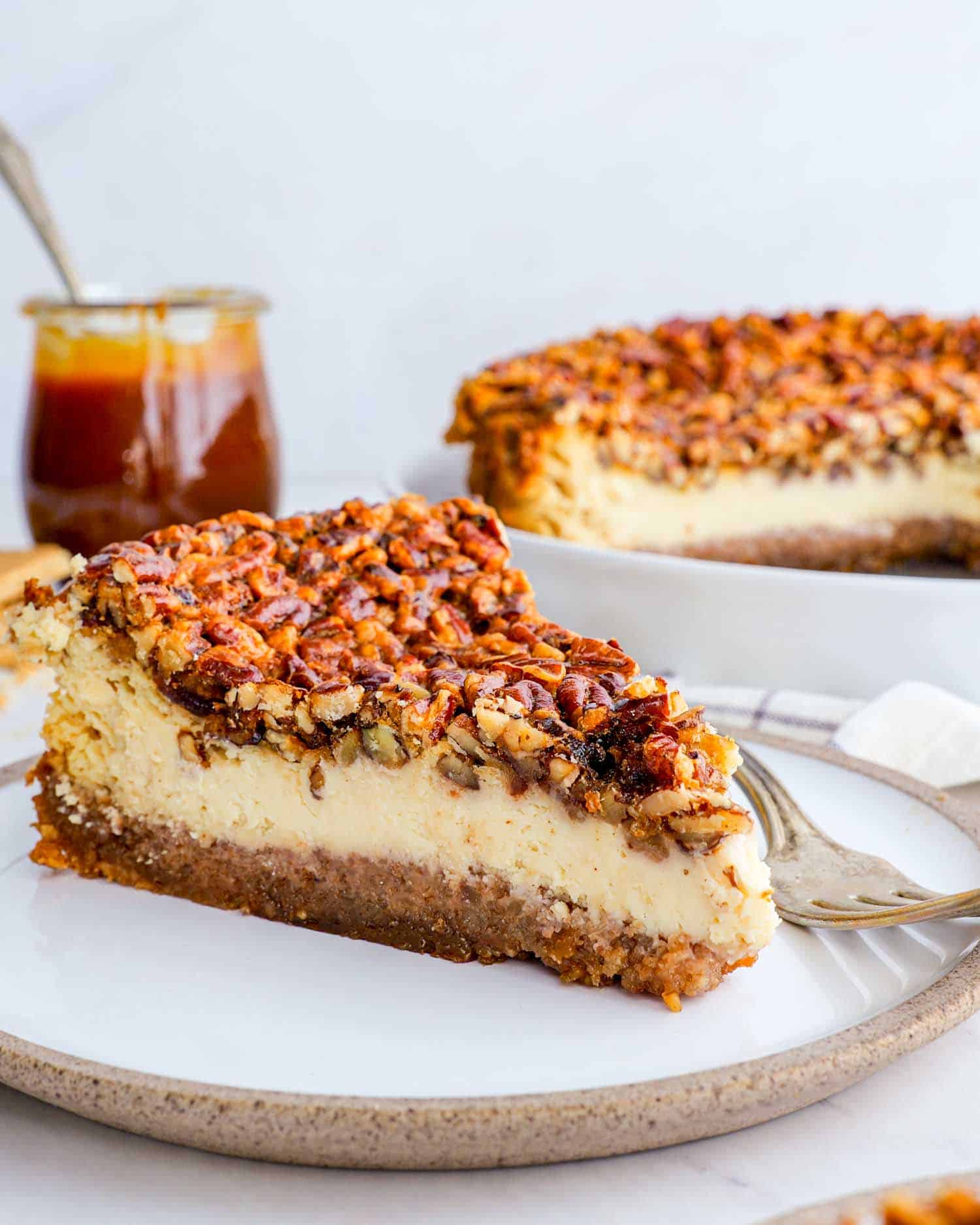 a slice of pecan pie cheesecake on a white plate with a fork.