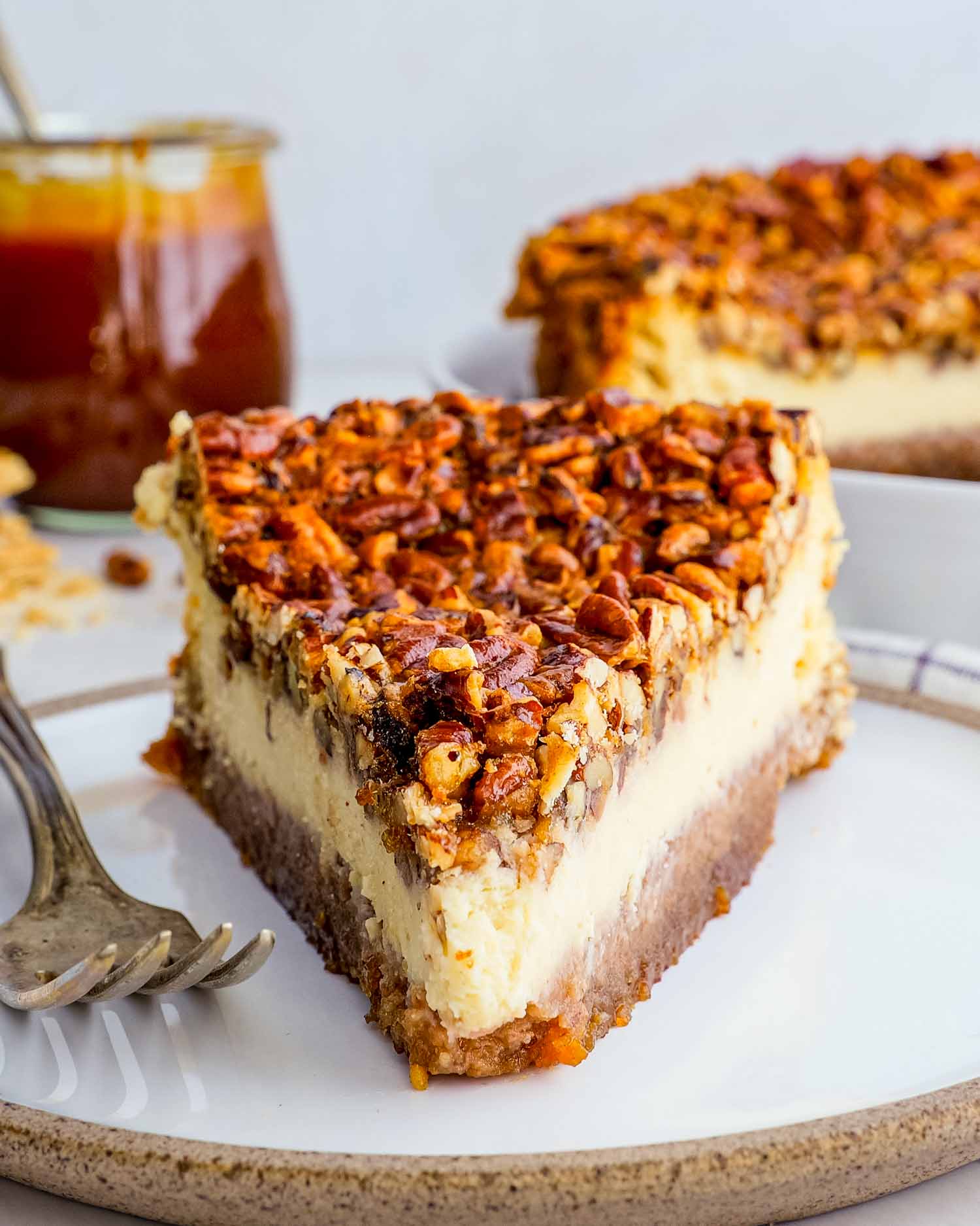 a slice of pecan pie cheesecake on a white plate with a fork.