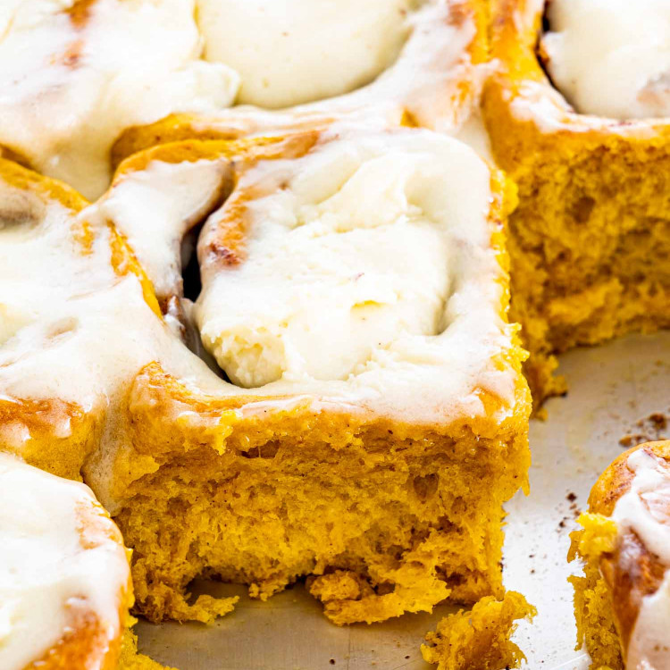 pumpkin cinnamon rolls with cream cheese icing in a baking pan.