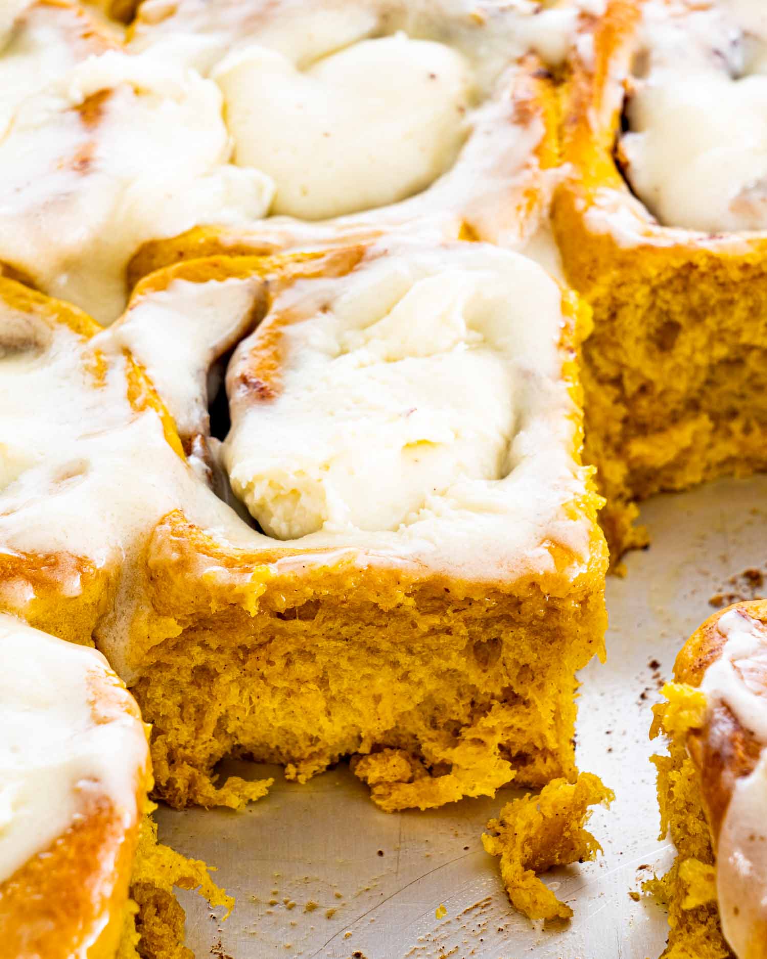 pumpkin cinnamon rolls with cream cheese icing in a baking pan.