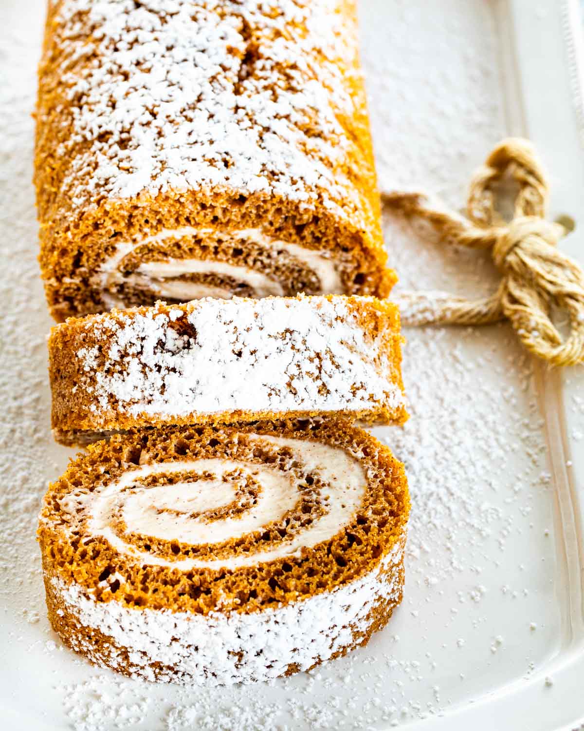 a pumpkin roll on a serving platter with a couple slices cut out.