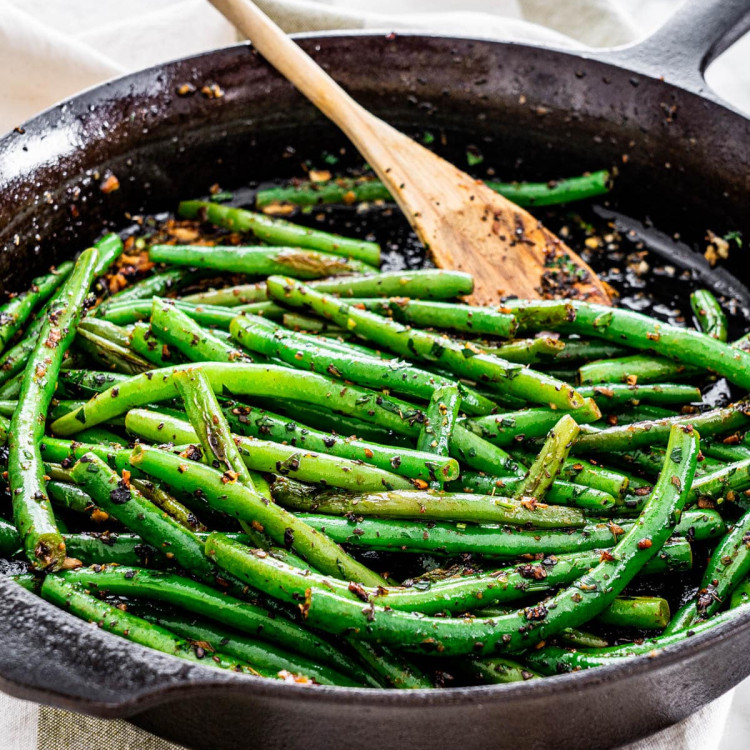 green beans in a skillet with a wooden spoon