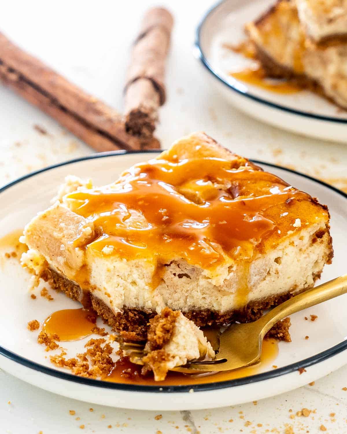 an apple pie cheesecake bar on a white plate drizzled with salted caramel.