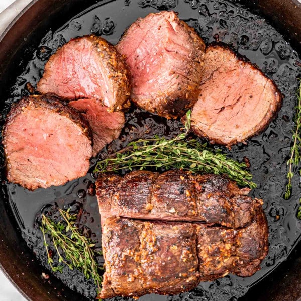 a beef tenderloin with half of it cut in slices in a cast iron skillet.