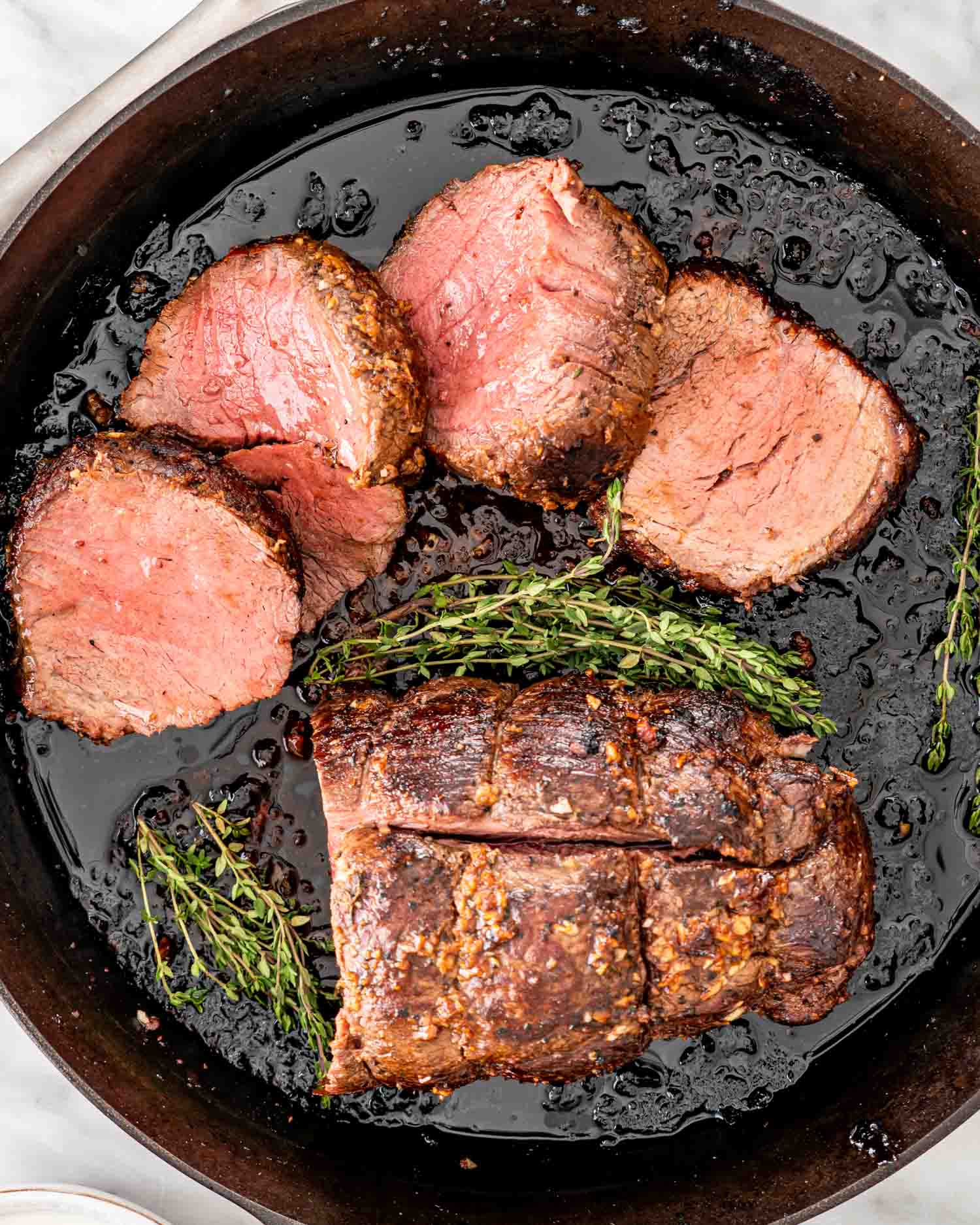 a beef tenderloin with half of it cut in slices in a cast iron skillet.