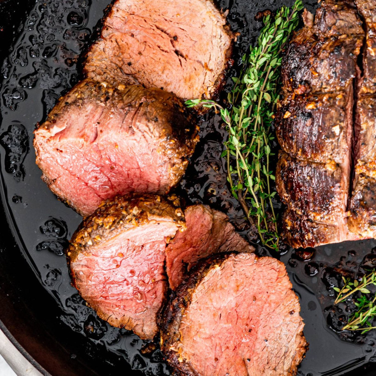 overhead shot of beef tenderloin sliced in a skillet with sprigs of thyme