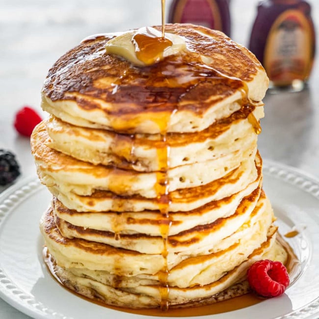 syrup being poured over a stack of buttermilk pancakes