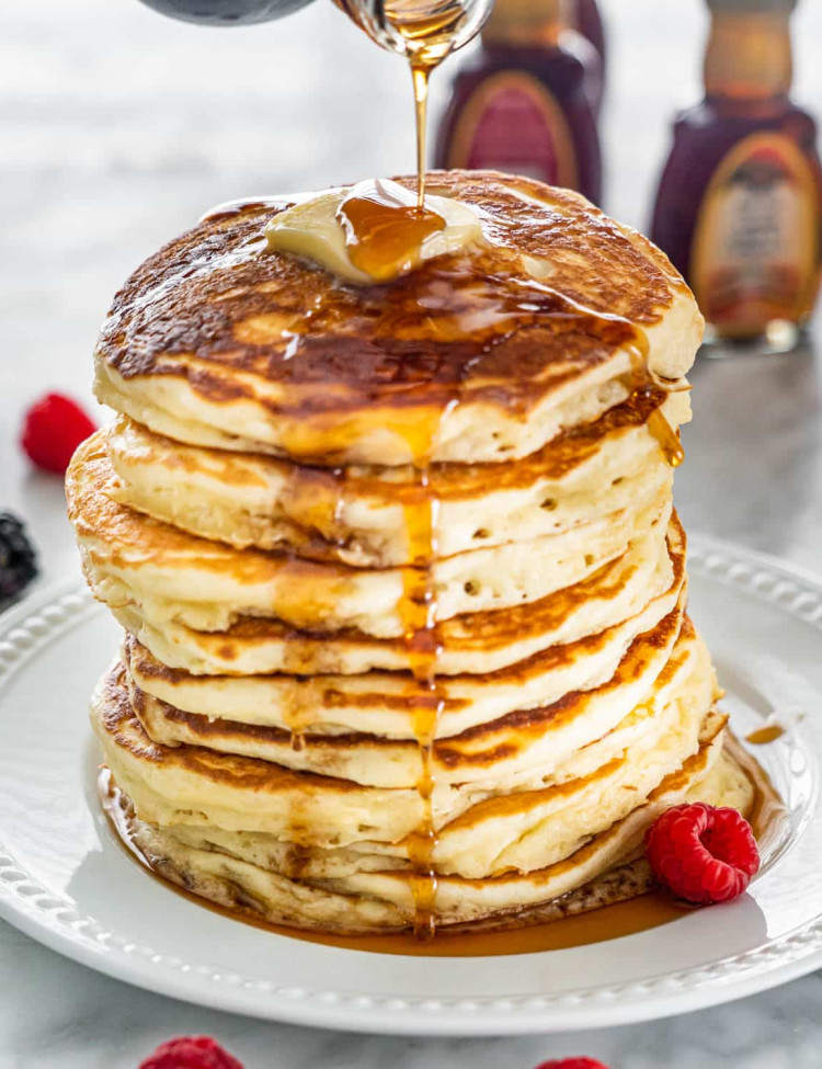 syrup being poured over a stack of buttermilk pancakes