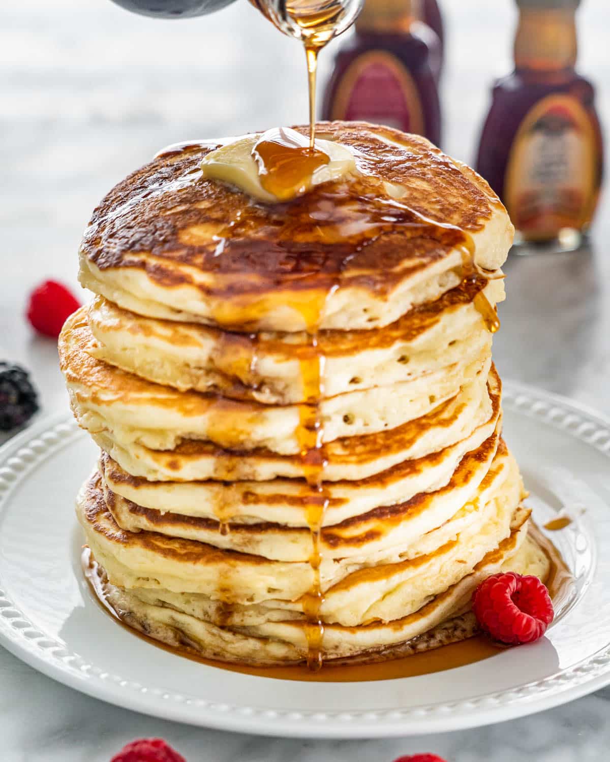 drizzling maple syrup over a stack of buttermilk pancakes