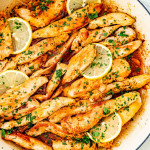 garlic butter chicken in a skillet garnished with parsley and lemon slices.