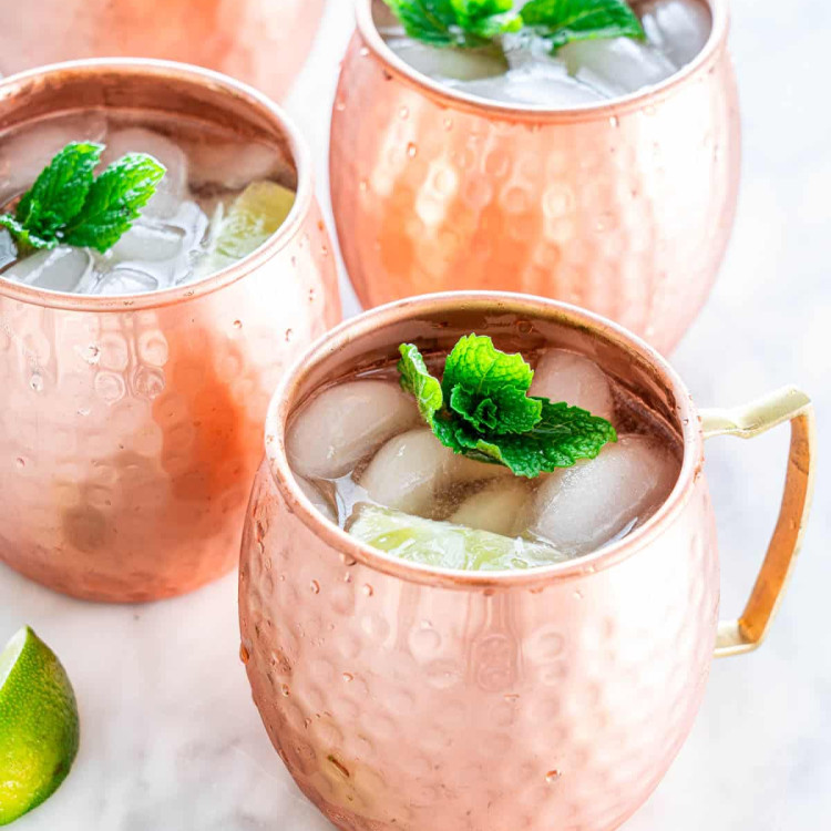 copper mugs filled with moscow mule cocktails topped with sprigs of mint
