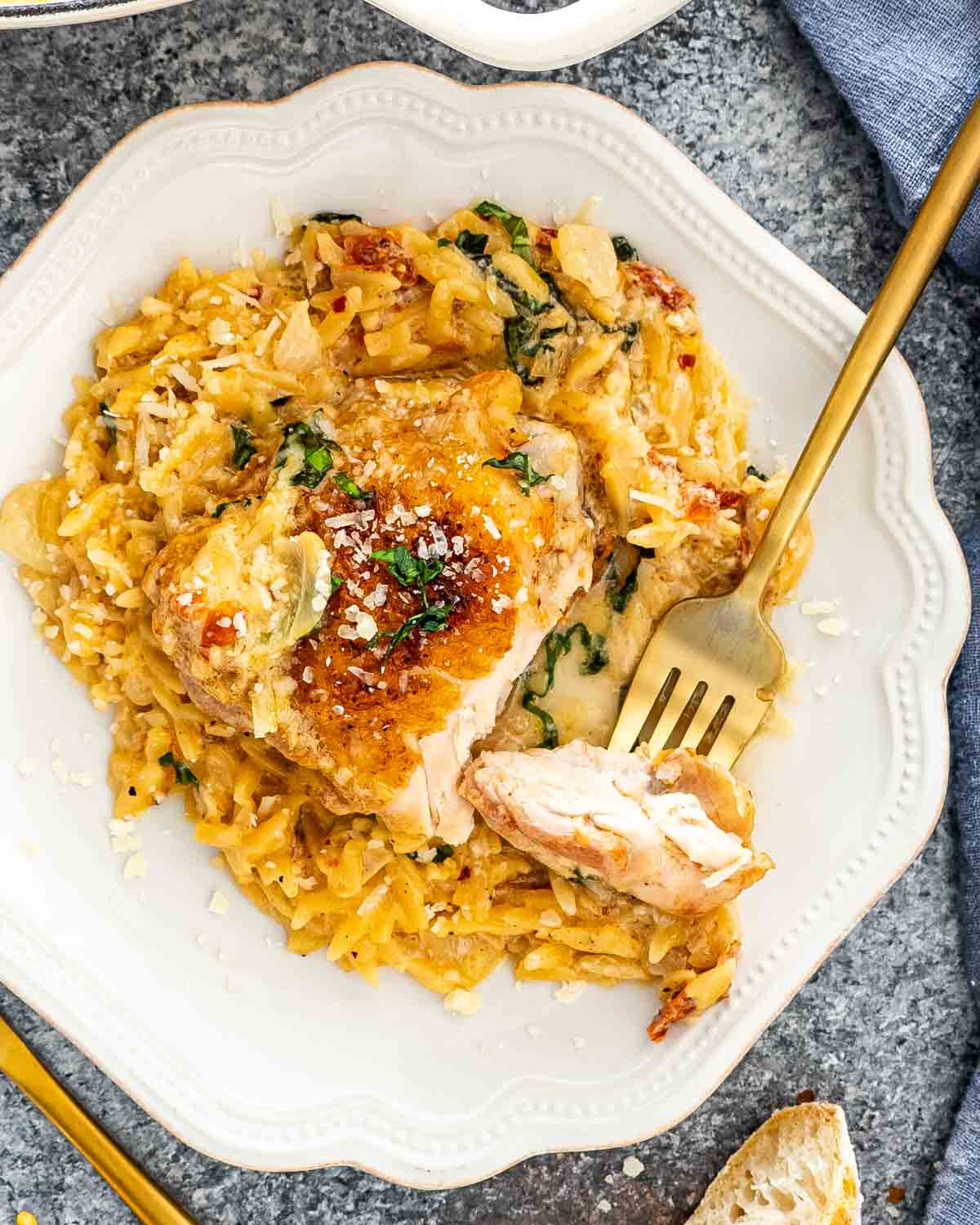 chicken thigh and orzo on a white plate with a fork holding a piece of chicken.