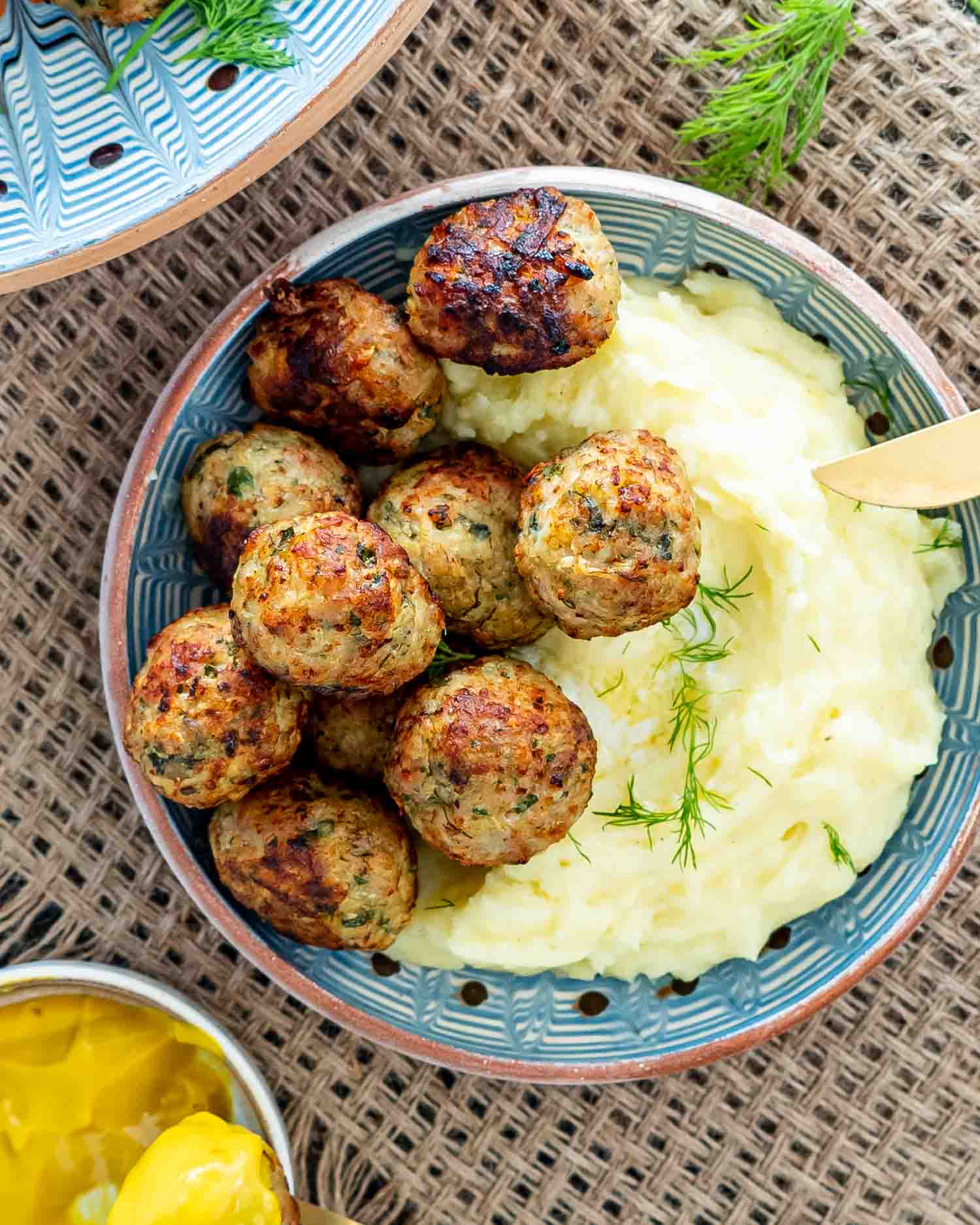 Romanian meatballs with mashed potatoes in a clay plate garnished with dill.