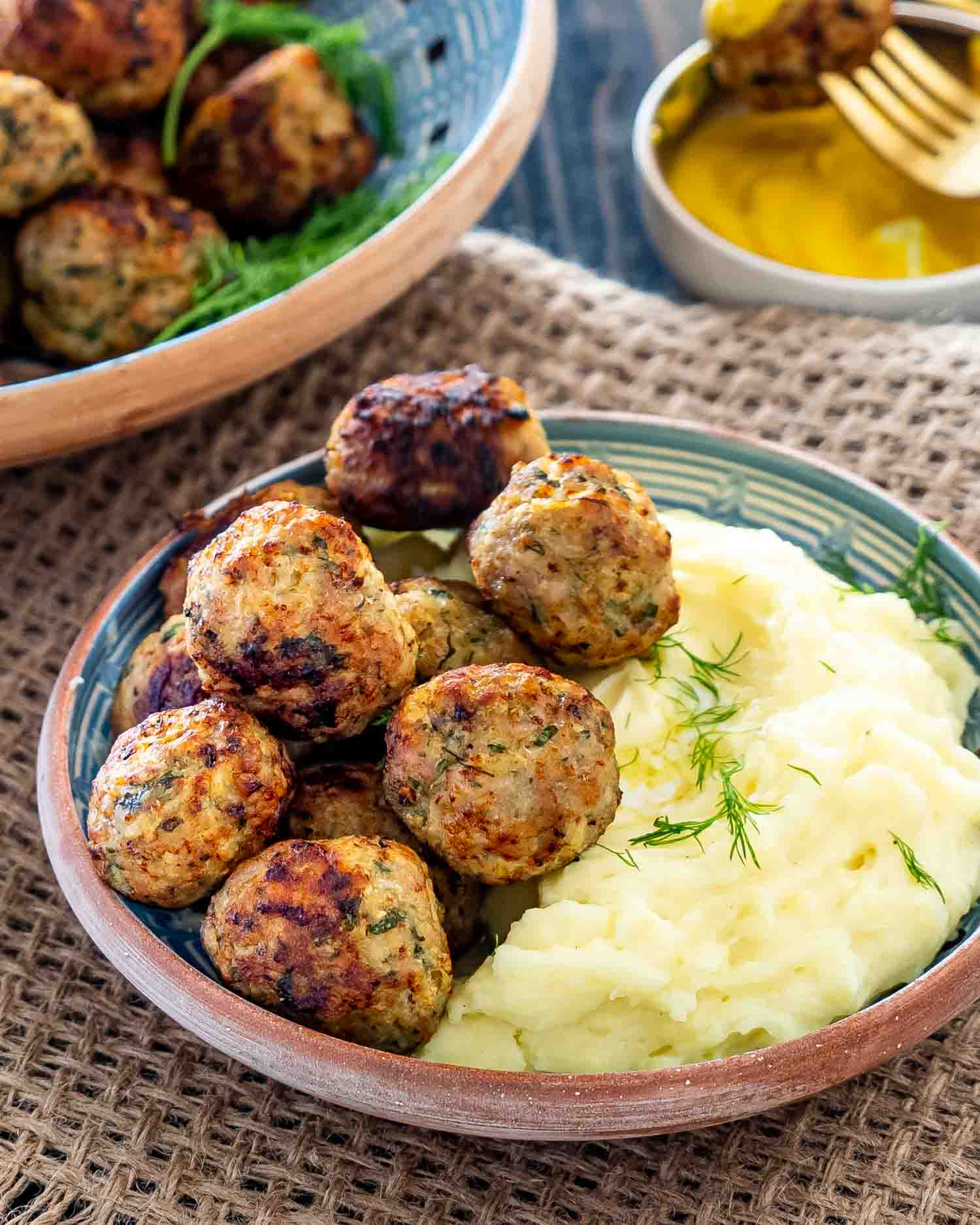 Romanian meatballs with mashed potatoes in a clay plate garnished with dill.