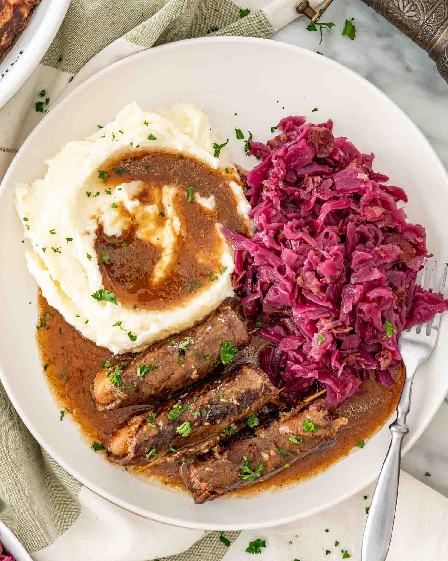 a plate with beef rouladen, mashed potatoes, gravy and german red cabbage.