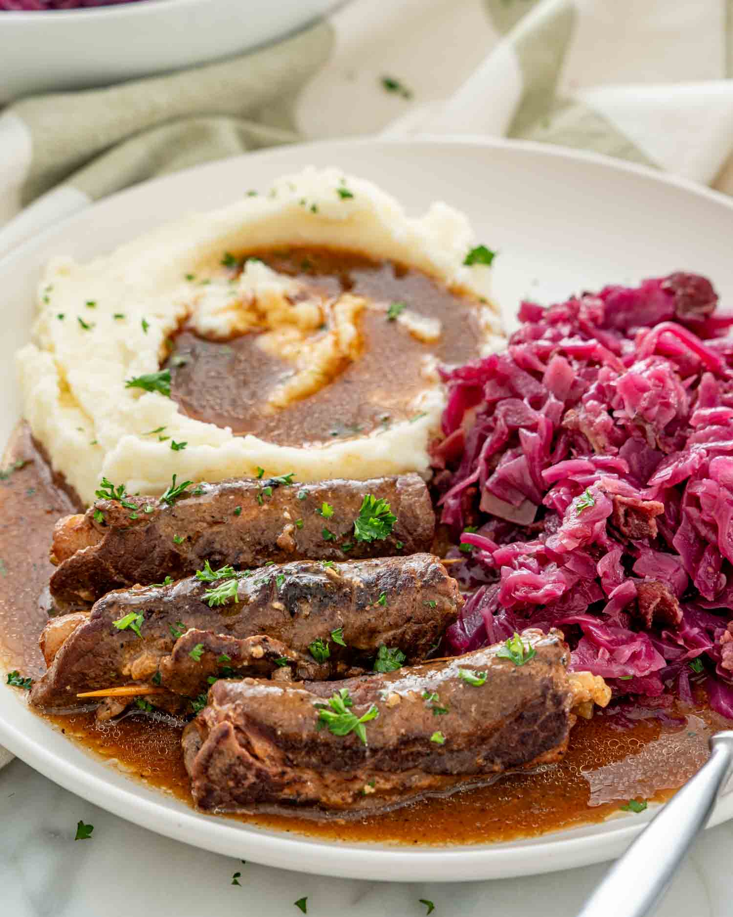 a plate with beef rouladen, mashed potatoes, gravy and german red cabbage.
