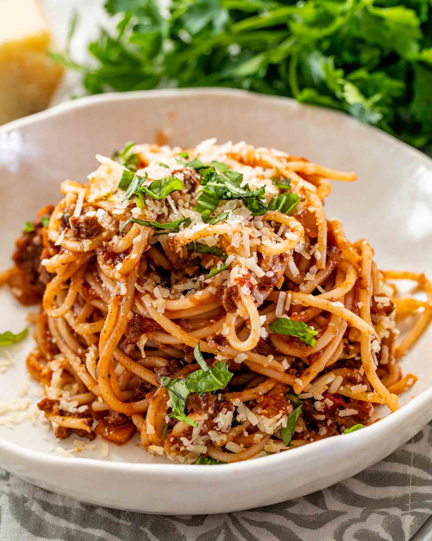 a serving of spaghetti bolognese in a white bowl garnished with parsley. 