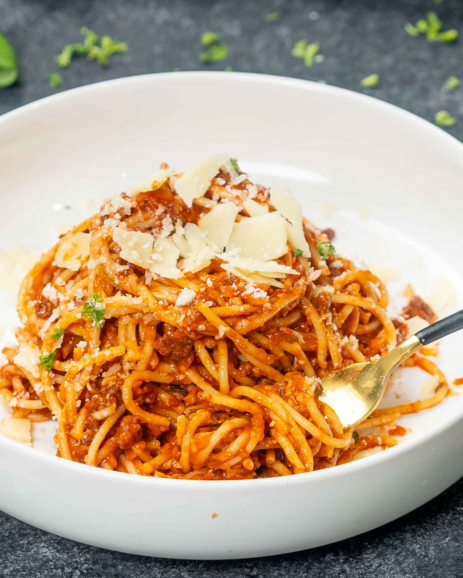 a serving of spaghetti bolognese in a white bowl garnished with parsley.