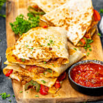 chicken fajita quesadillas on a cutting board with salsa and garnished with parsley.