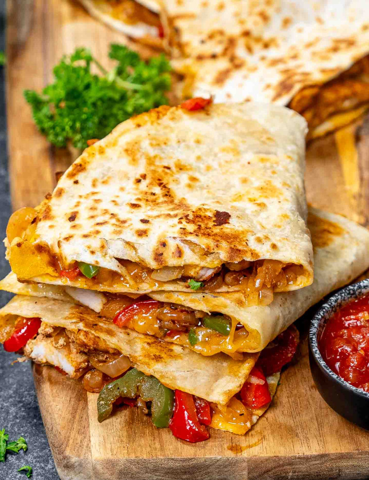 chicken fajita quesadillas on a cutting board with salsa and garnished with parsley.