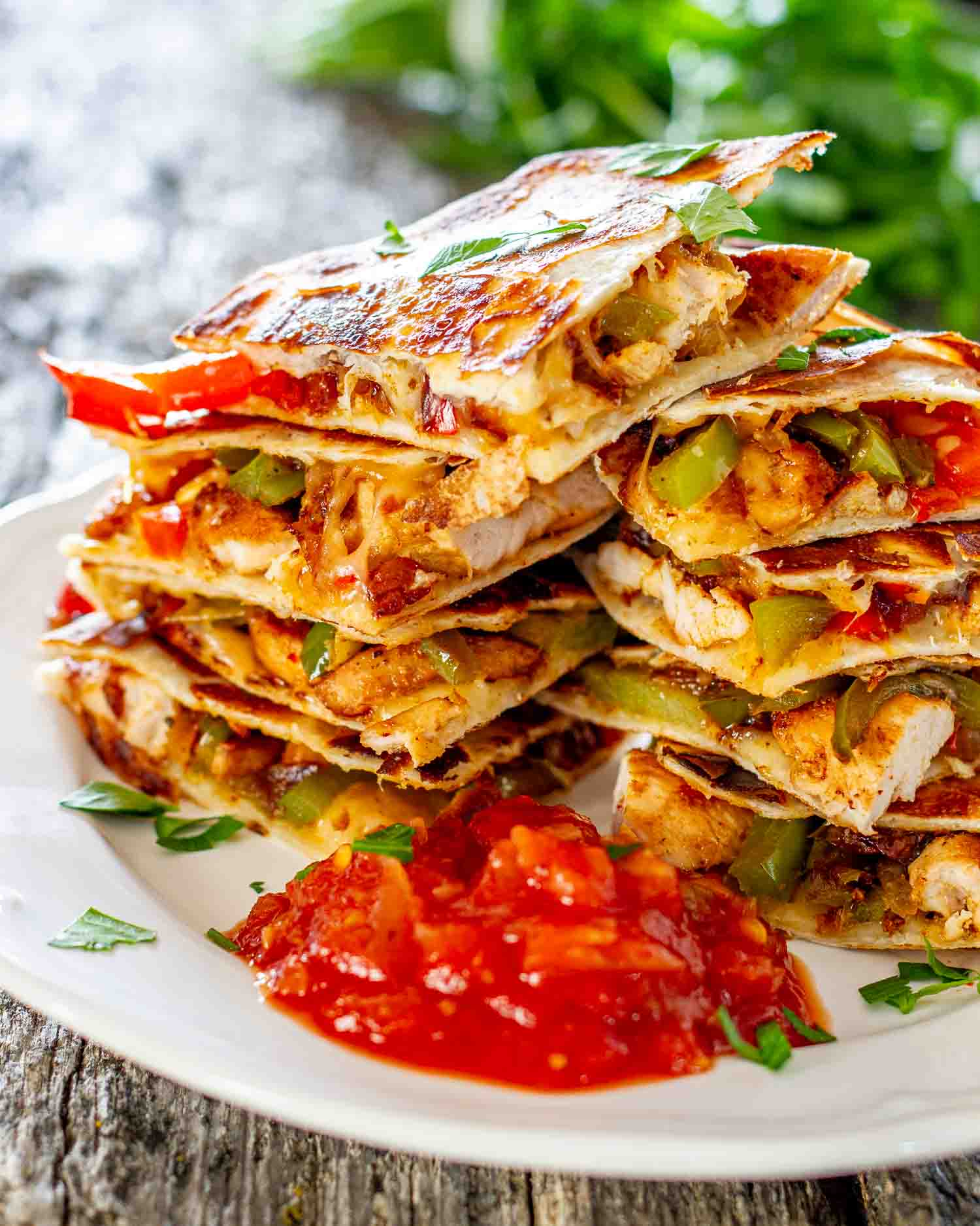 a stack of chicken fajita quesadillas with some salsa on a plate and garnished with parsley.
