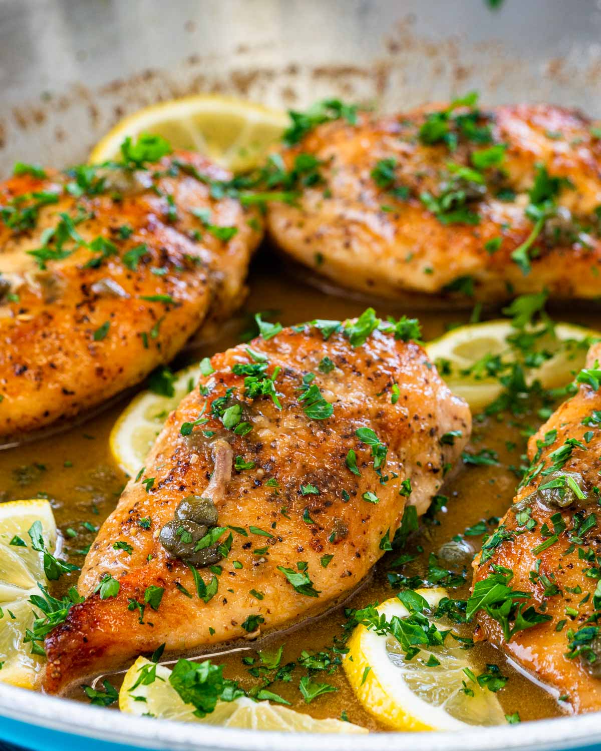 freshly made chicken piccata in a skillet garnished with parsley and lemon wedges.