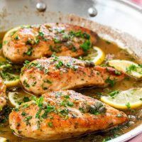 freshly made chicken piccata in a skillet garnished with parsley and lemon wedges.