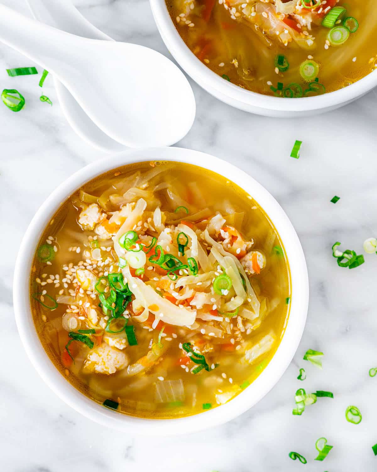 overhead shot of two white bowls filled with egg roll soup garnished with green onions and sesame seeds