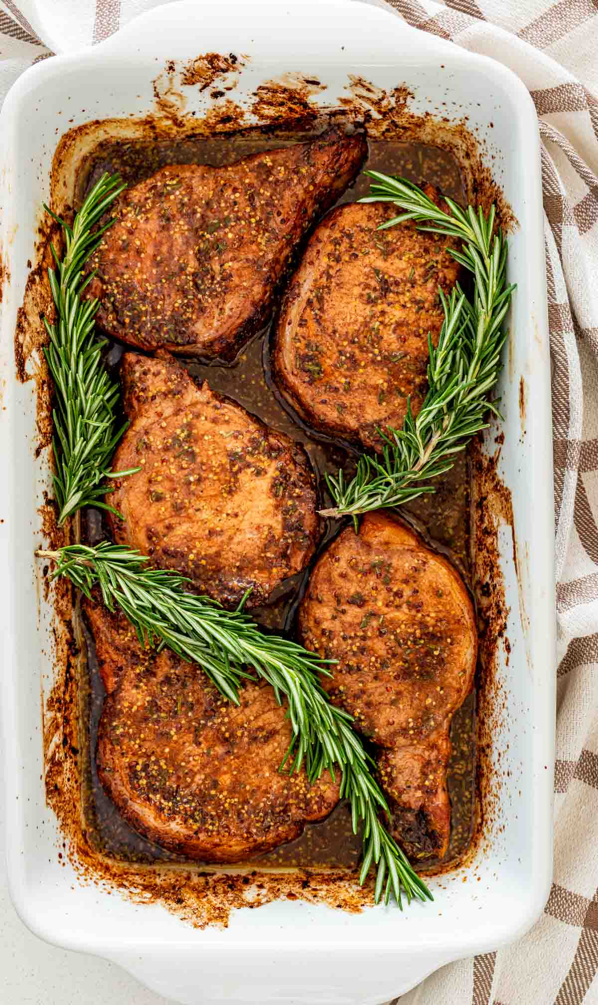 mustard balsamic pork chops in a white casserole dish garnished with rosemary.