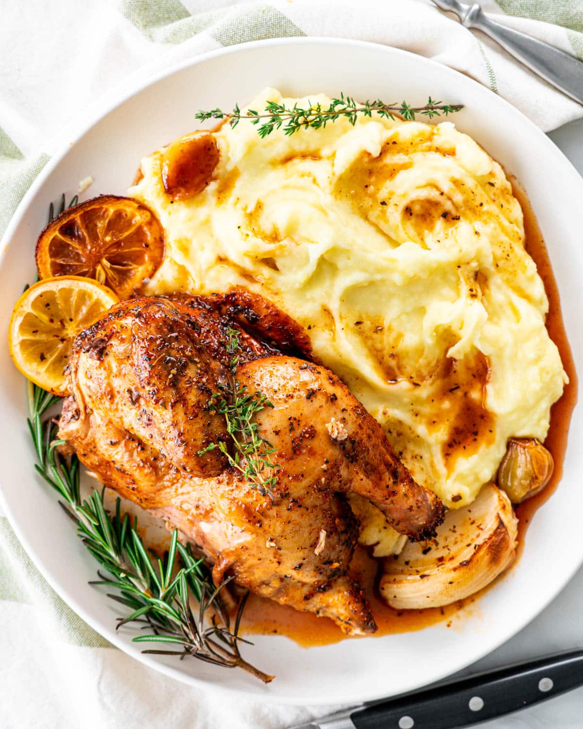 half a cornish hen with mashed potatoes, pan juice and garnished with rosemary and lemon slices