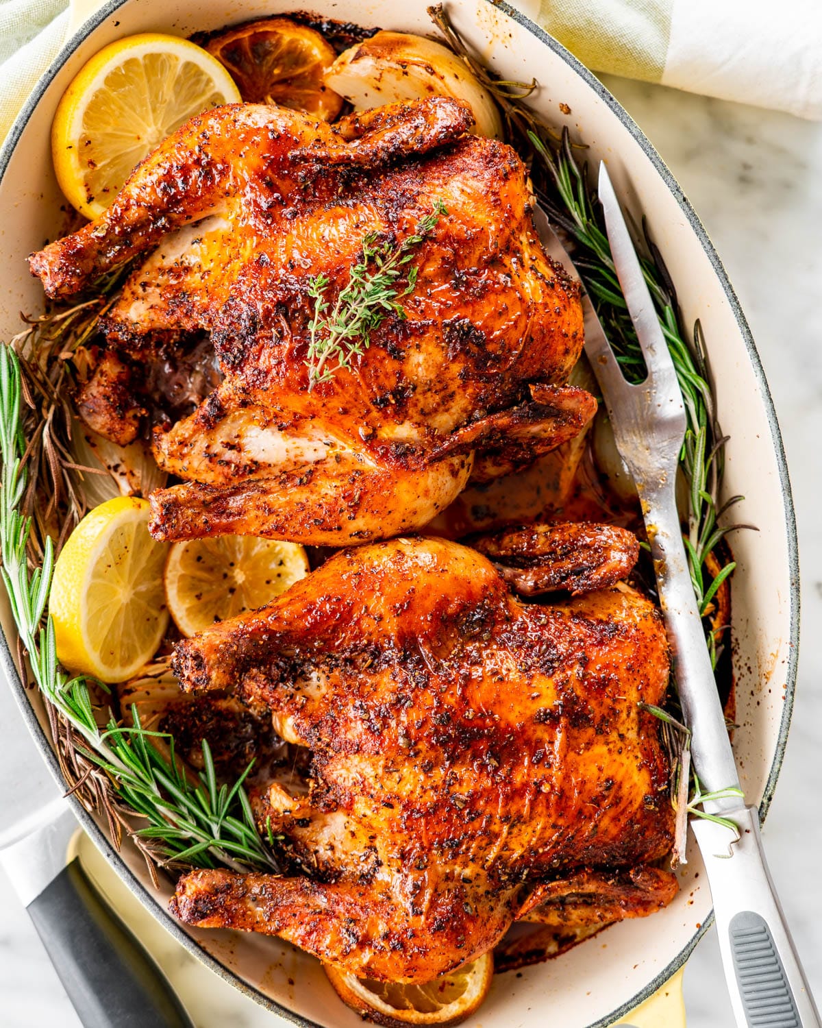overhead shot of roasted cornish hens in a roasting pan garnished with rosemary or lemon slices