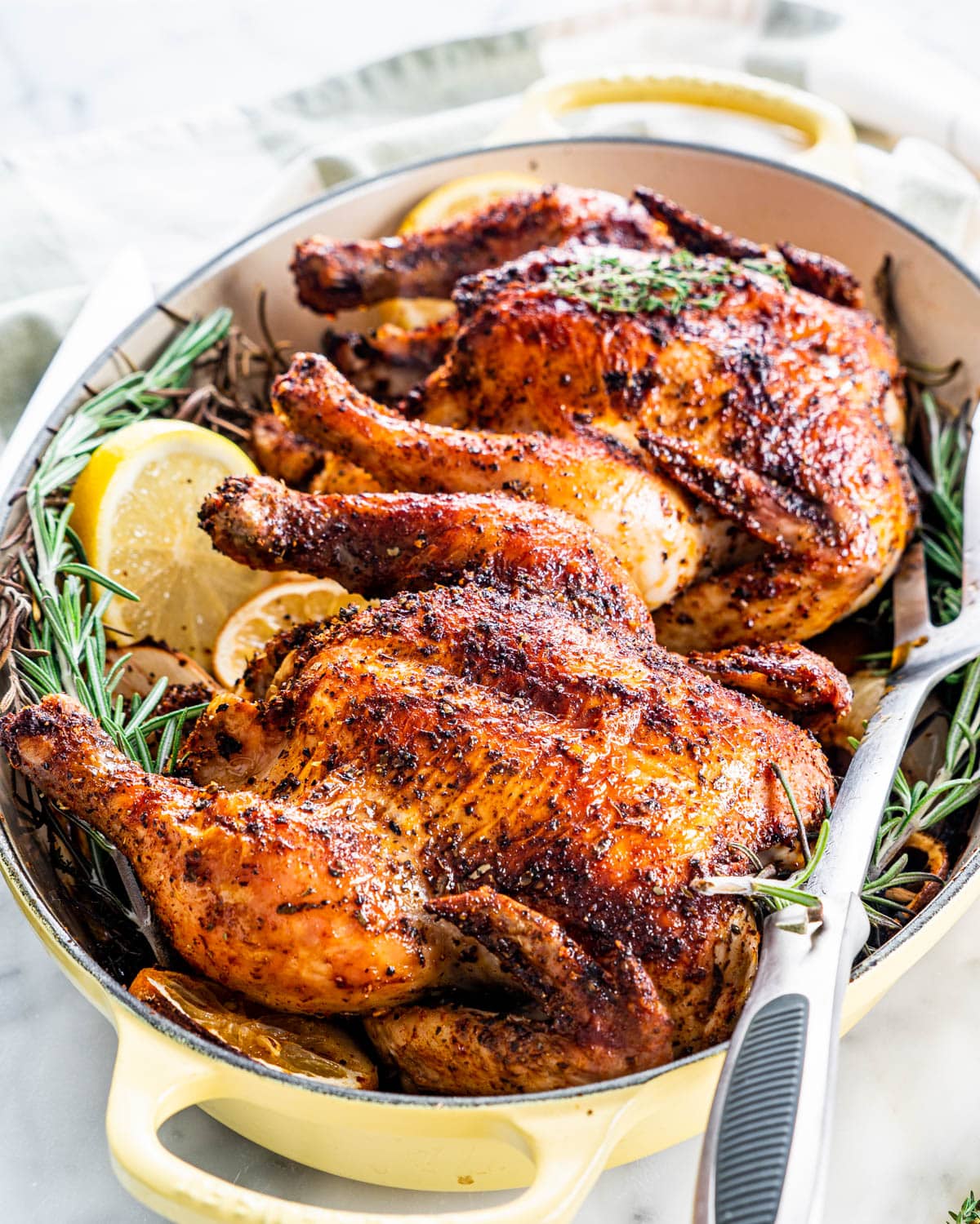 two roasted cornish hens in a roasting pan garnished with rosemary and lemons