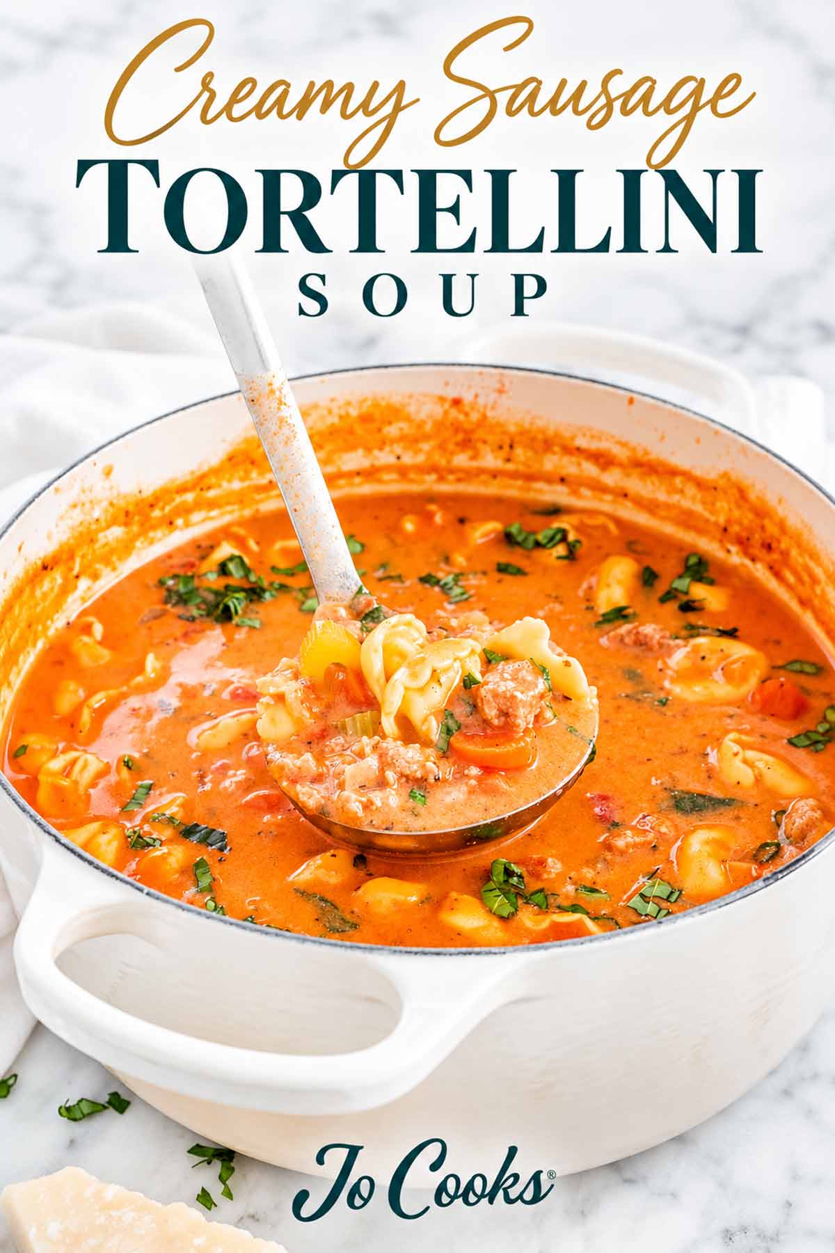 Ladleful of creamy sausage tortellini soup above a white Dutch oven, with gold and teal lettering and Jo Cooks logo.