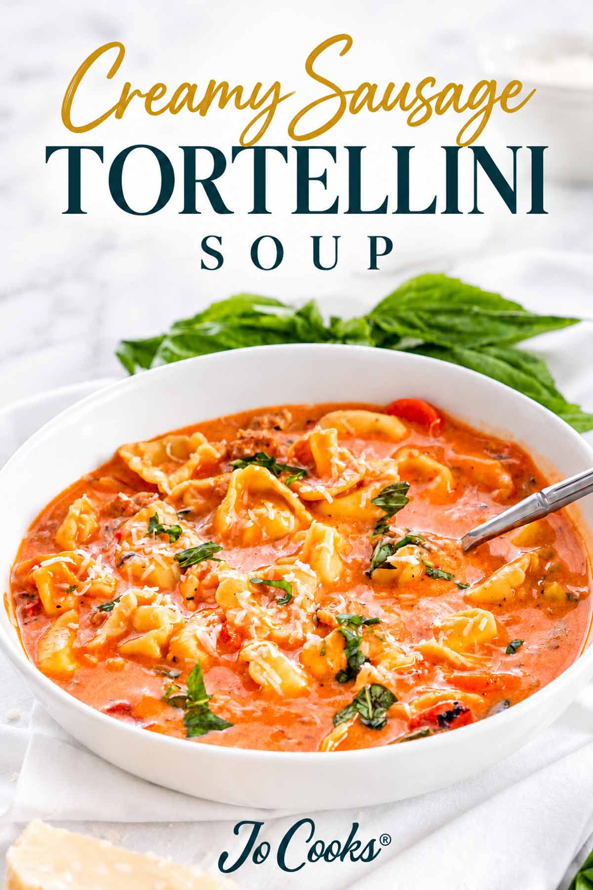 White bowl of creamy sausage tortellini soup topped with Parmesan and basil beneath the recipe title and Jo Cooks logo.