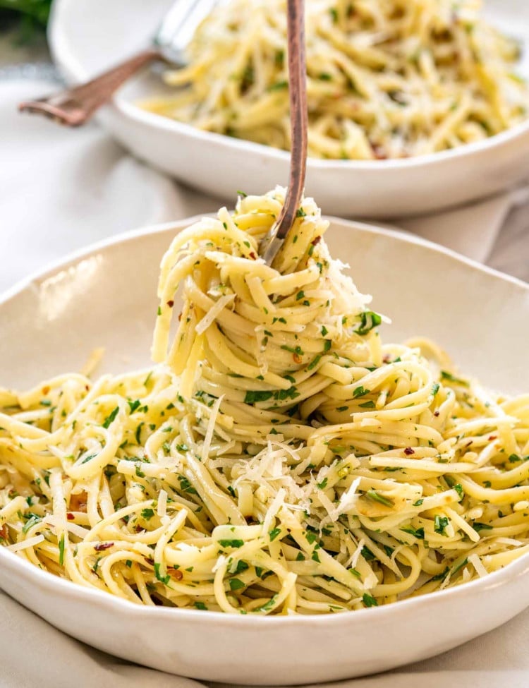 a fork twirling linguini in a plate full of aglio e olio.