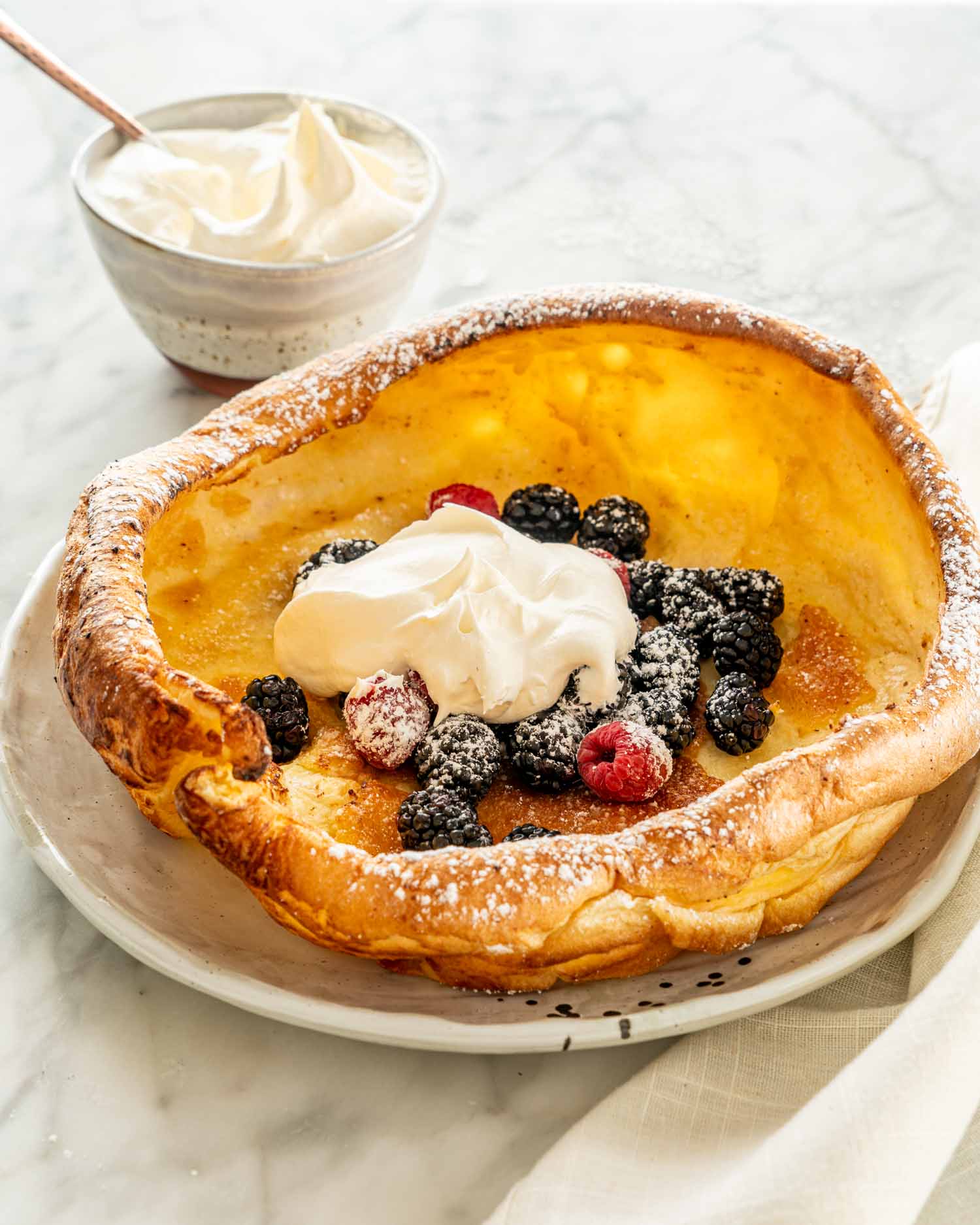 dutch baby pancake on a plate topped with berries and a dollop of whipped cream.