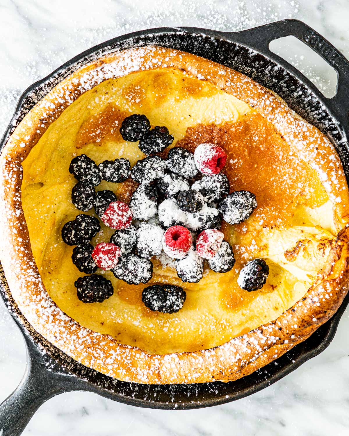 overhead shot of a dutch baby pancake in a skillet topped with berries and powdered sugar
