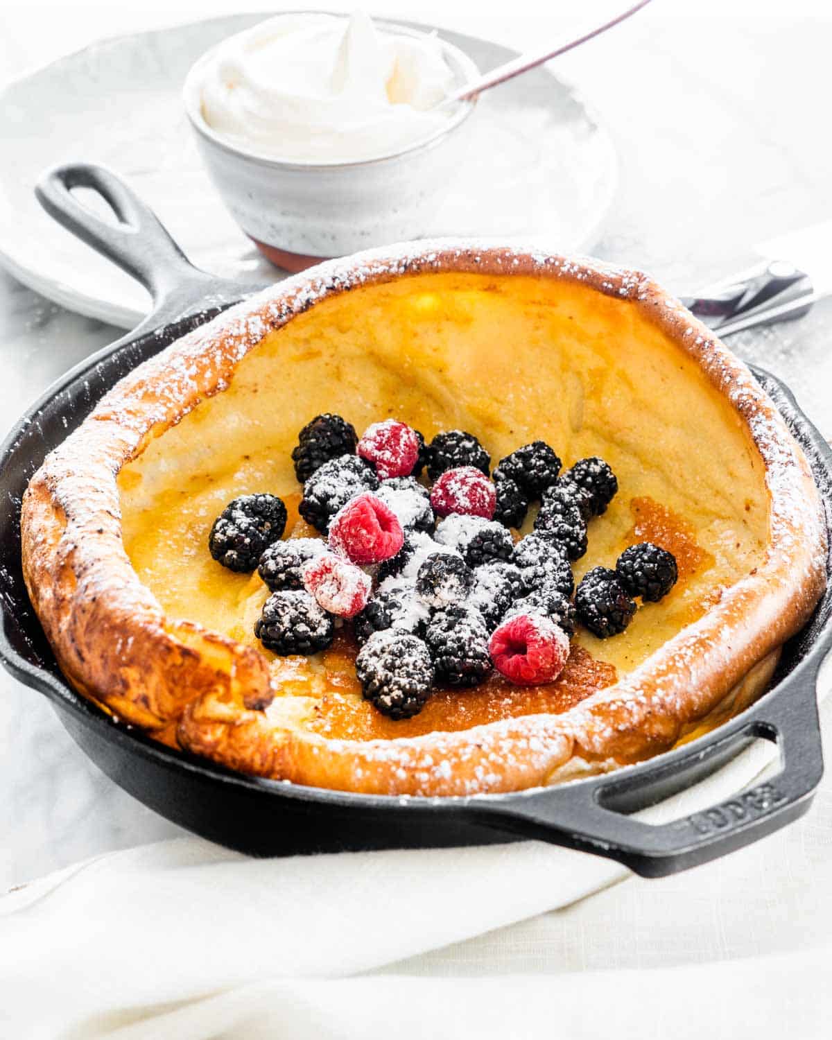 a dutch baby pancake in a skillet fresh out of the oven topped with berries and powdered sugar