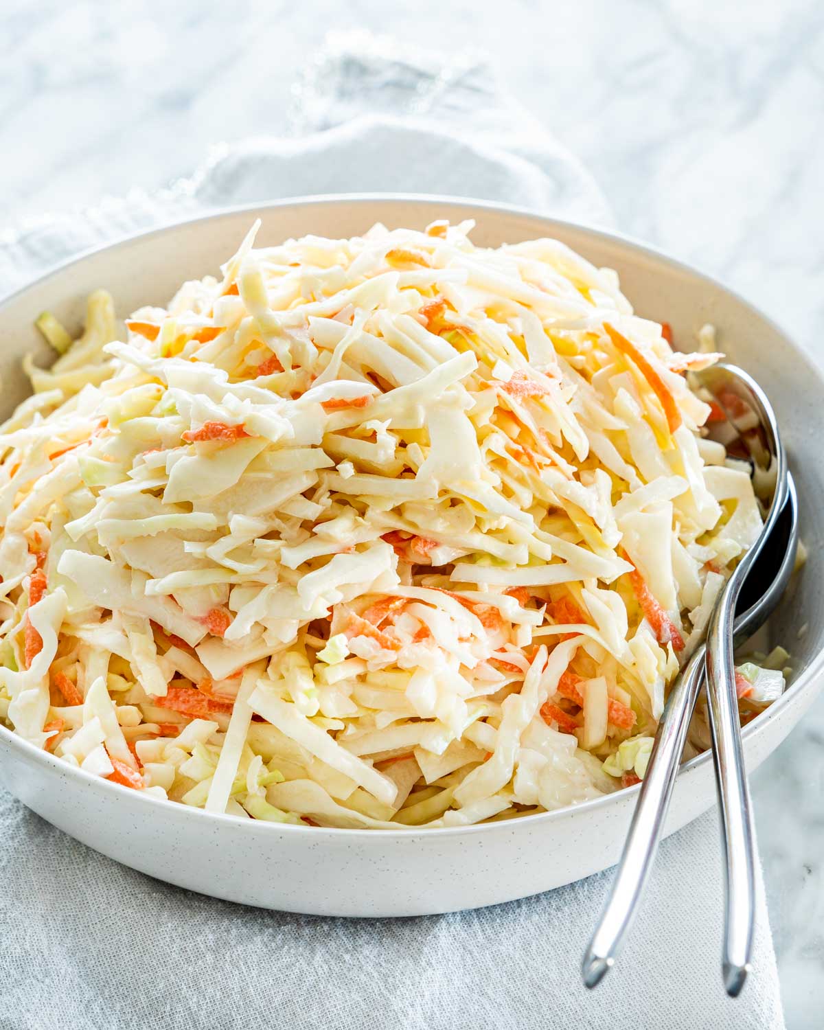 a bowl with coleslaw in it and two serving spoons