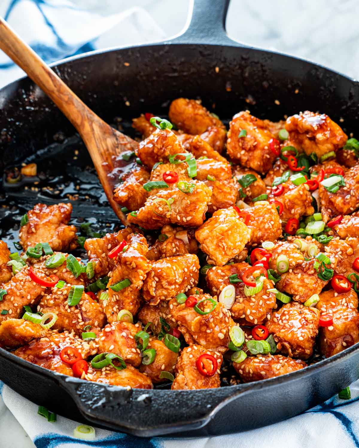 korean fried chicken in a skillet garnished with red chilis and green onions