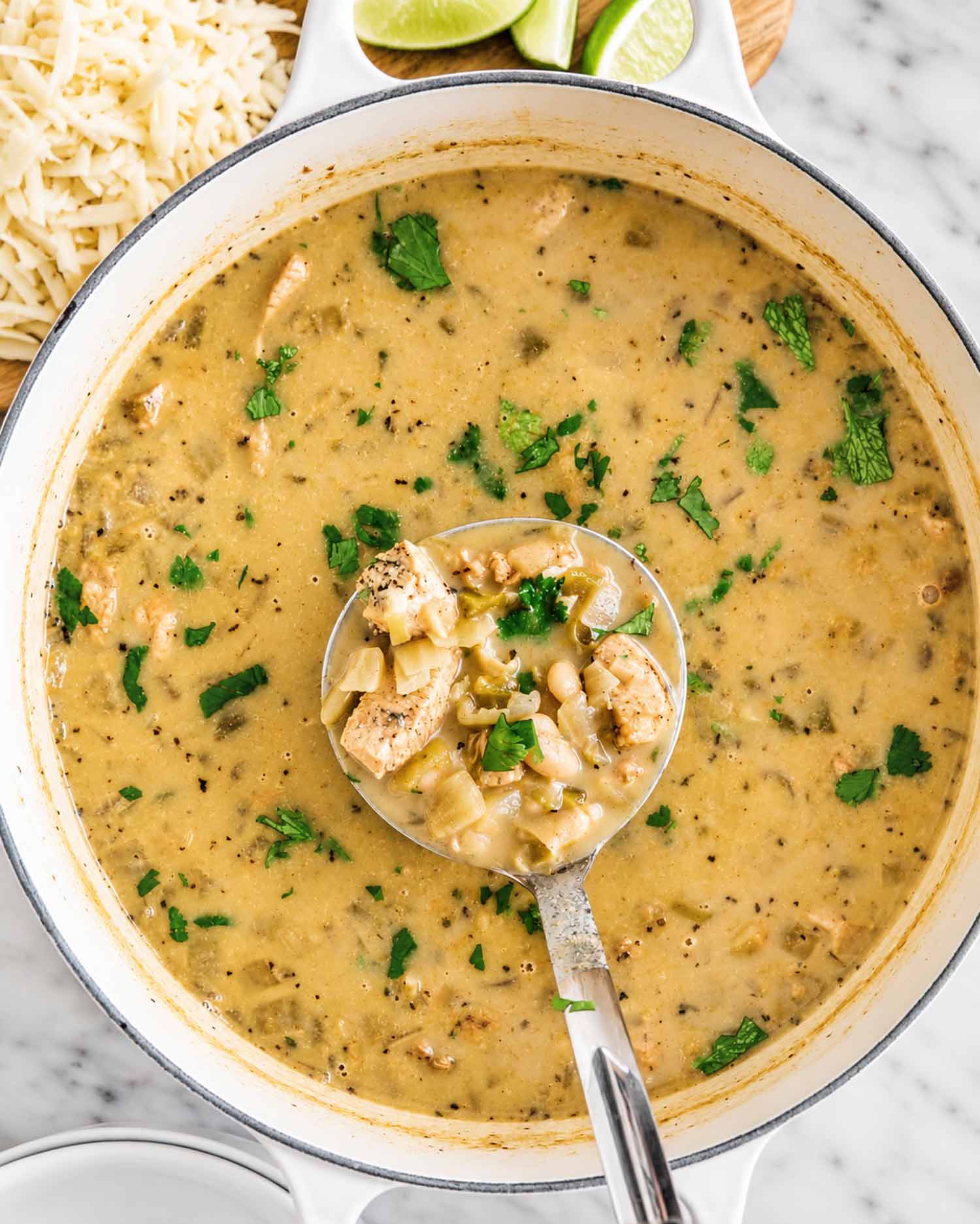 A ladle filled with chicken, cannellini beans, and green chiles rests in a pot of creamy white chicken chili.