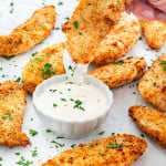 a hand dipping a chicken tender in ranch dressing